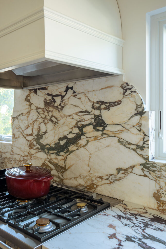 Gas cooktop with full-height marble backsplash and custom hood