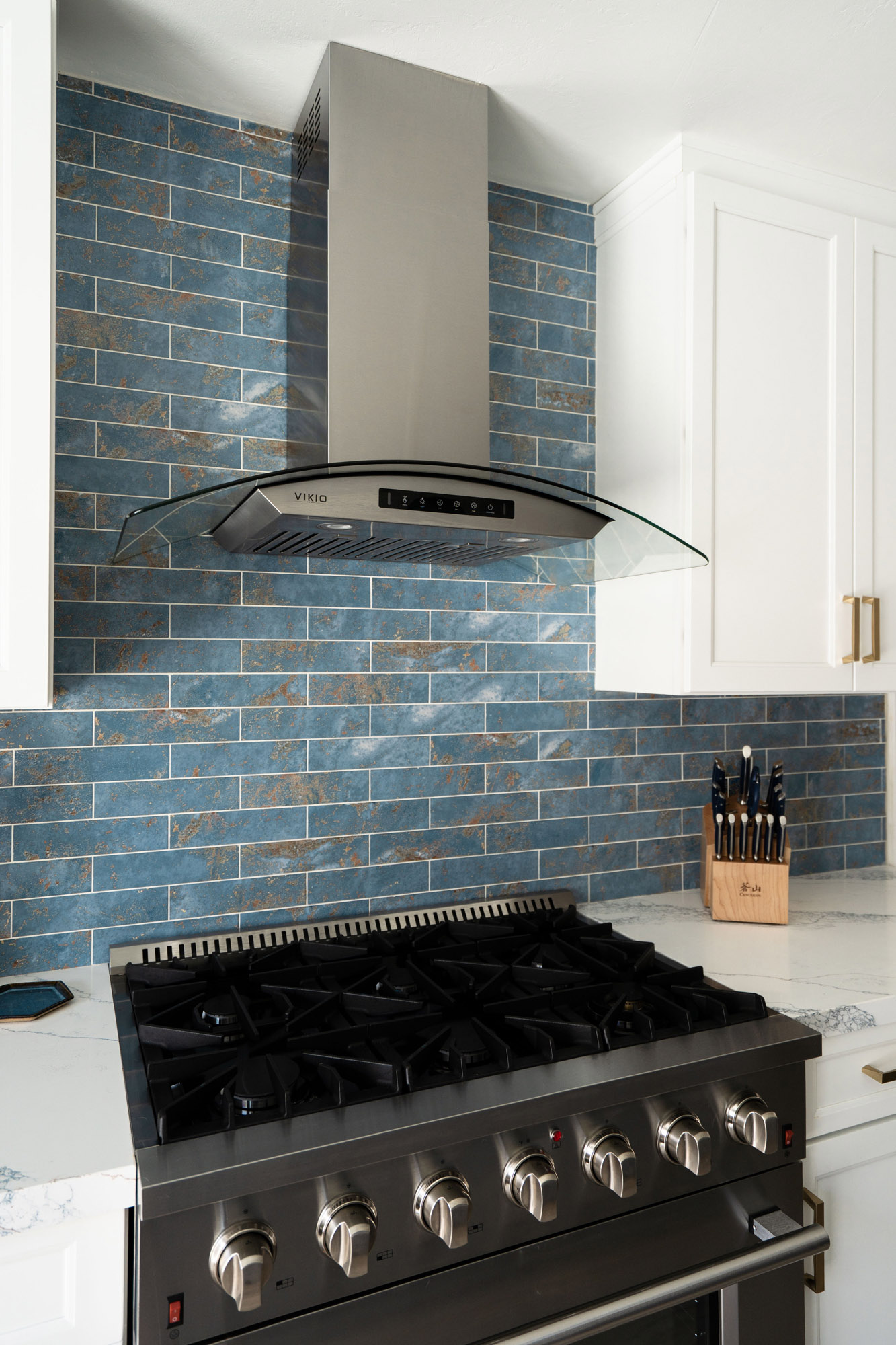San Diego Kitchen Remodel, blue-coastal Modern stainless steel range hood with curved glass, surrounded by coastal blue tile and white cabinetry in Clairemont, San Diego.